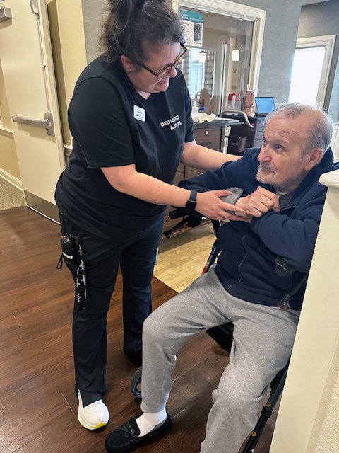 An employee assisting an elderly man during a wellness check-up at a senior community.