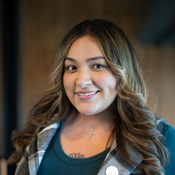 Karina Orona Perez, Memory Care Director at The Madison Senior Living, smiling in a professional indoor headshot wearing a teal top and plaid vest.