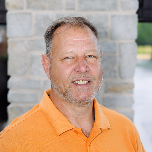 Bob Maple, Plant Operations Director at The Madison Senior Living, smiling in front of a stone building while wearing an orange polo shirt.