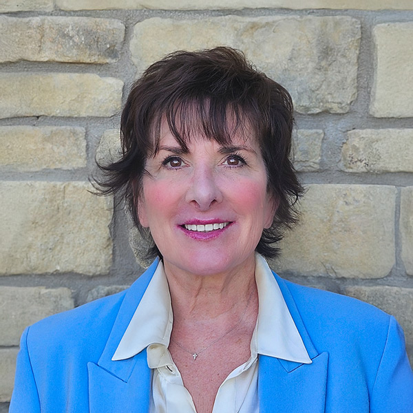 Heather Gray, Senior Living Director at The Madison Senior Living, smiling in front of a stone wall while wearing a light blue blazer and cream blouse.