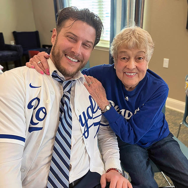 Senior resident wearing a Royals shirt smiles alongside a man in a Royals jersey and tie.