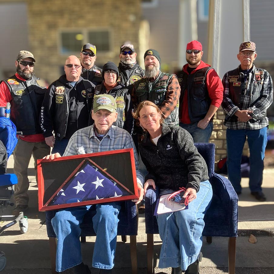 A senior man proudly holds a framed, folded flag while surrounded by others in matching vests.