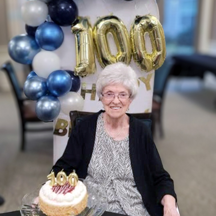 A senior woman celebrates her 100th birthday with decorations and cake.