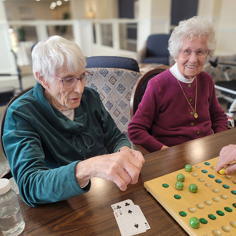 Two senior residents enjoy a tabletop game and conversation at The Madison Senior Living.