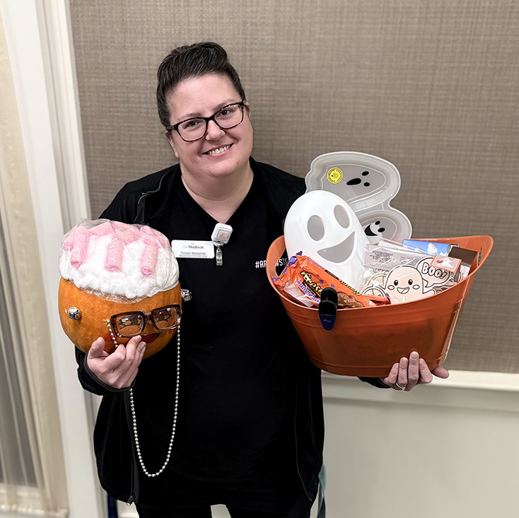 A woman on the Madison team smiles, displaying a decorated pumpkin and a basket of Halloween treats.