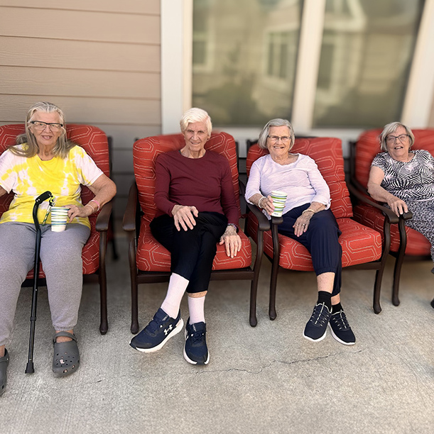 Four senior residents relax in a comfortable outdoor seating area on a sunny day.